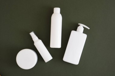 Alüminyum kozmetik kavanozu ve koyu yeşil arka planda üç farklı beyaz şişe, kozmetik ürünleri doğal kozmetik ambalajlarını taklit ediyor. Güzellik ürünleri konsepti.