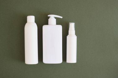 Koyu yeşil arka planda üç farklı beyaz şişe. Kozmetik ürünleri Doğal Kozmetik Paketleme. Güzellik ürünleri konsepti.