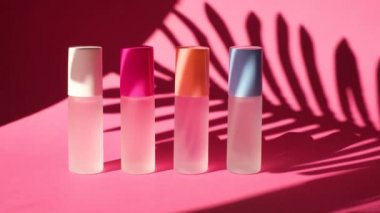 Pembe geometrik podyumlarda parfümlü birkaç sprey şişe üzerinde sallanan bir palmiye yaprağının gölgesi parfüm sunumu için kompozisyon sahnede dört parfüm şişesi, pembe arka plan.