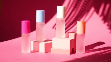 Pembe geometrik podyumlarda parfümlü birkaç sprey şişe üzerinde sallanan bir palmiye yaprağının gölgesi parfüm sunumu için kompozisyon sahnede dört parfüm şişesi, pembe arka plan.