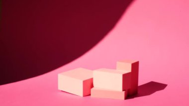 Pembe arka planda çeşitli pembe geometrik podyumlar, hoş gölgeler ve güneş ışığı, sallanan bir palmiye yaprağının gölgesi.