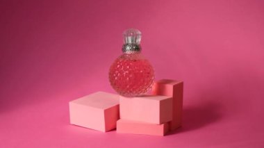Geometrik podyumlar ve gümüş kapaklı pembe kristal parfüm şişesi, sert gölgeler, güneş ışığı, pembe arka planda refleksler ve parıltı, palmiye yaprağı gölgesi.