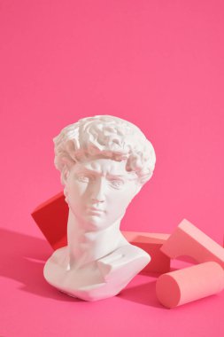 Beyaz dekoratif heykel büstü ve pembe arka plan geometrik şekilli birkaç pembe geometrik bardak altlığı. Sergi podyumu, ürün sunumu platformu