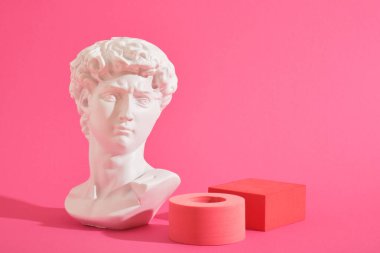 Beyaz dekoratif heykel büstü ve pembe arka plan geometrik şekilli birkaç pembe geometrik bardak altlığı. Sergi podyumu, ürün sunumu platformu
