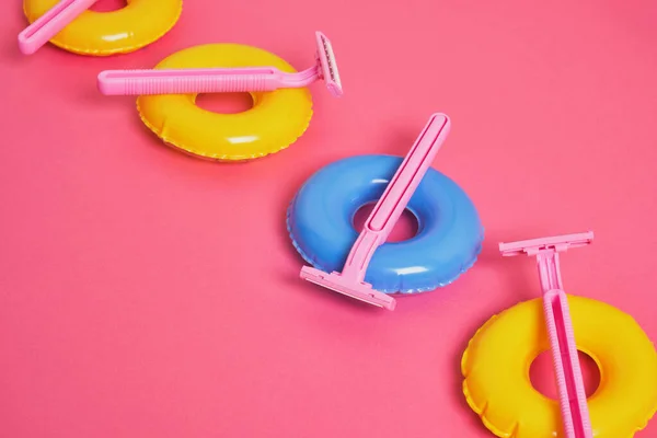 pink disposable razors on small toy balloons on pink background, body hair removal before beach vacation concept, summer vacation and depilation