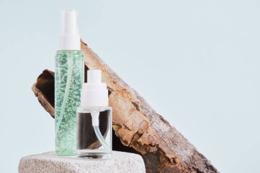 Ağaç kabuğu ve iki boş şişe, beton bir podyumun üzerinde beyaz bir kapakla açık mavi arka planda, kozmetik şişeler, yeşil jel ve parfümlü bir şişe