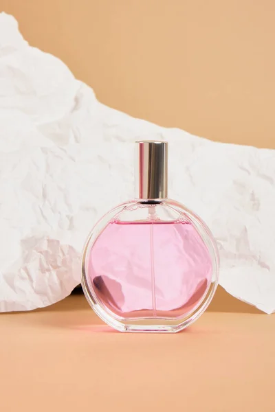 round perfume bottle with a silver cap on a background of white crumpled paper, pink perfume in a transparent glass packaging, mock up a simple shape of a perfume bottle