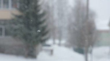 Şehre kar yağışı, pencereden manzara. Kar yığınları. Karlı ağaçlar, arabalar, binalar ve yol seçici odak noktası