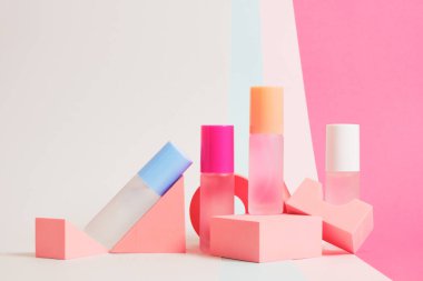 Parlak bir arkaplanda farklı renklerde parfüm şişeleri, pembe geometrik stantlarda parfüm şişeleri.