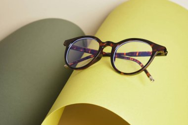 Yuvarlanan kağıt üzerindeki gözlük, geometrik arkaplan, yeşil renkler, gri arka plan, görüş testi konsepti, optik mağazasındaki güzel moda aksesuarları