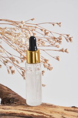 Gri arka planda tahta bir kütükte jel serumlu pipet şişesi. Ürününüz için model arka plan.