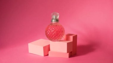 Geometrik podyumlar ve gümüş kapaklı pembe kristal parfüm şişesi, sert gölgeler, güneş ışığı