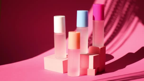 Відтінок від погойдувального пальмового листа на декількох скляних пляшках з парфумами на рожевих геометричних подіумах — стокове відео