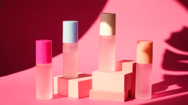 Schaduw van een zwaaiend palmblad op verschillende spuitglazen flessen met parfum op roze geometrische podia — Stockvideo