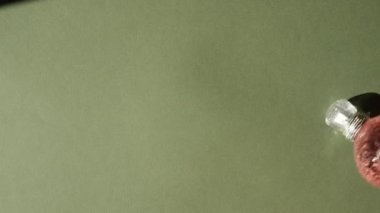Gümüş kapaklı pembe kristal parfüm şişesi, sert gölgeler, güneş ışığı, refleksler ve yeşil arka planda parlama