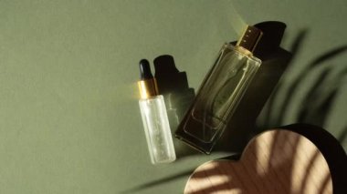 Pipet ve şeffaf parfüm şişesi ve yeşil arka planda palmiye yaprağı gölgesi olan damlama şişesi. Üst taraf seçici odak noktası, sert gölge ve ışık.