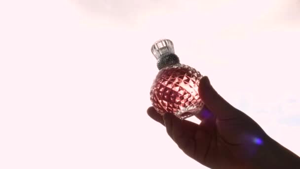 Rosa Kristallflasche Spray mit Parfüm in der Hand auf dem Hintergrund des Fensters und Sonnenlicht — Stockvideo