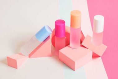 Parlak bir arkaplanda farklı renklerde parfüm şişeleri, pembe geometrik stantlarda parfüm şişeleri.