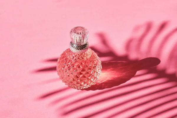 ピンクの背景にシルバーボトルの香水のクリスタルボトル ヤシの葉からの影 ピンクのトイレの水 女性の香水 — ストック写真
