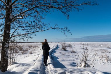 Aydınlık ve karlı, donmuş sulak arazide, patikada bir kadın.
