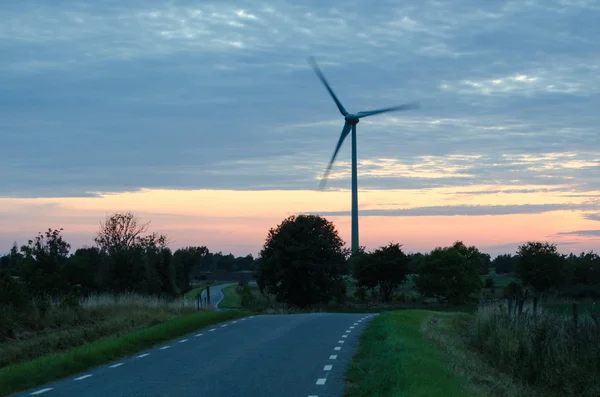 Wind turbine by a winding road at late evening — Stock Photo, Image