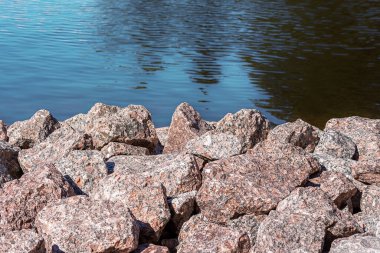 Kıyıda mavi bir su yüzeyine karşı büyük pembe granit yığını..