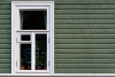 Koyu yeşil tahta levhalardan yapılmış bir duvarın arka planında beyaz çerçeveli dikdörtgen pencere. Dünya serisinin penceresinden.