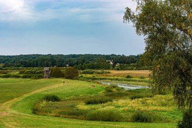Nehirli bir manzara, biçilmiş bir çayır ve güneşli bir sonbahar gününde eski bir yel değirmenine giden bir yol..