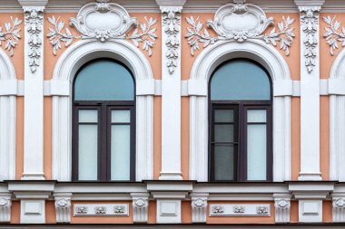Kahverengi ahşap çerçeveli iki kemerli pencere, beyaz sıva kaplı pembe bir duvara karşı. St. Petersburg 'un bir dizi penceresinden.