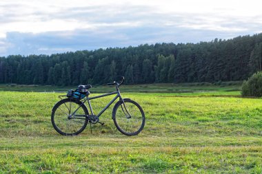 Walking bike stands on a path in a field against the background of a forest and sky with clouds on an autumn day.