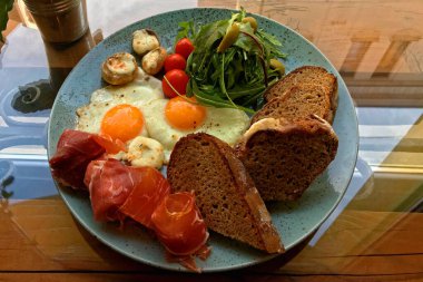 Breakfast of scrambled eggs with ham, vegetables and toasted slices of black bread on a blue plate.