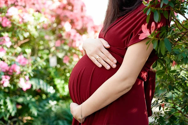 Young woman in maternity dress holds hands on belly