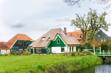 Güzel geleneksel çiftlik evi (inşaat stiline 'stolpboerderij' veya Haubarg) sazdan çatılı ve yumuşak yeşil saçaklı. Ön girişte büyük bir çiçek açan ağaç. Ana evin ön cephesi yeşil ve beyaza boyanmış. Ahırda. 