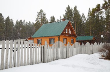 Kırsal evin arkasında bir çit. Köydeki bahar karla karışık yağmur