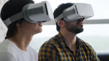 Evde kulaklıkla sanal gerçeklik oyunu oynayan genç bir çift. Mutlu insanlar online oyun için sanal gerçeklik kulaklığı kullanıyor. Erkek ve kadın gülümsüyor, ev eğlencesi teknolojisinin tadını çıkarıyor. Yavaş çekim