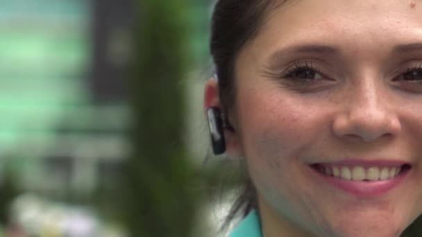 Mujer de negocios con dispositivo bluetooth mirando a la cámara sonriendo — Vídeos de Stock