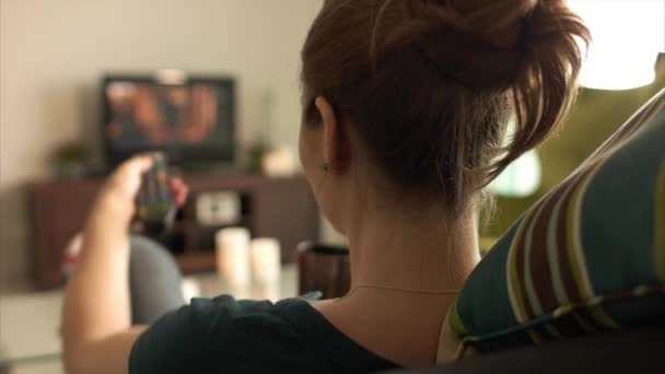 Женщина отдыхает на диване смотря фильм по телевизору с дистанционным — стоковое видео