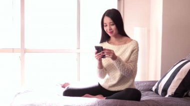 Evde yatakta Smartphone ile Asyalı kadın için sakin ol
