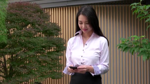 Mladá asijská žena SMS zpráva s Smartphone nedaleko úřadu úsměv — Stock video