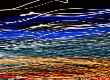 Işık dalgası boyası. Gece şehri neon ışıltısı etkisi hızlanıyor. Sarı, mavi ve altın enerji çizgileri soyut sanat arkaplanı. Hızlı araba trafiği akşam veya alacakaranlıkta uzun süre bulanıklaşır.