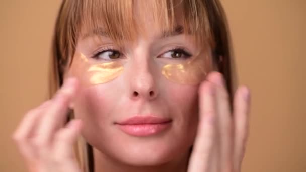 Hermosa mujer sonriente con el pelo corto en parches de ojo de oro mirando en la cámara y sonriendo sobre fondo de oro colorido. Concepto de belleza — Vídeo de stock