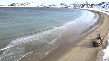 Karlı kış mevsiminde deniz kıyısında boğulan eski batık balıkçı gemilerinin hava manzarası. Görüntü. Rusya 'nın Teriberka kentindeki karlı sahil kıyısındaki soğuk sulardaki harabe teknenin hava görüntüsü.