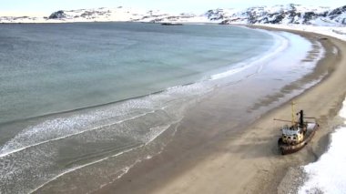 Karlı kış mevsiminde deniz kıyısında boğulan eski batık balıkçı gemilerinin hava manzarası. Görüntü. Rusya 'nın Teriberka kentindeki karlı sahil kıyısındaki soğuk sulardaki harabe teknenin hava görüntüsü.
