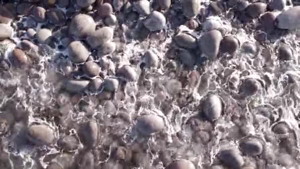 Vol aérien d'hiver au-dessus des vagues roulant sur le rivage de l'océan arctique avec des pierres rondes, vagues océaniques à la tempête — Video