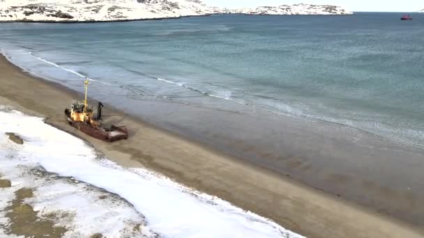 Karlı kış mevsiminde deniz kıyısında boğulan eski batık balıkçı gemilerinin hava manzarası. Görüntü. Rusya 'nın Teriberka kentindeki karlı sahil kıyısındaki soğuk sulardaki harabe teknenin hava görüntüsü. — Stok video