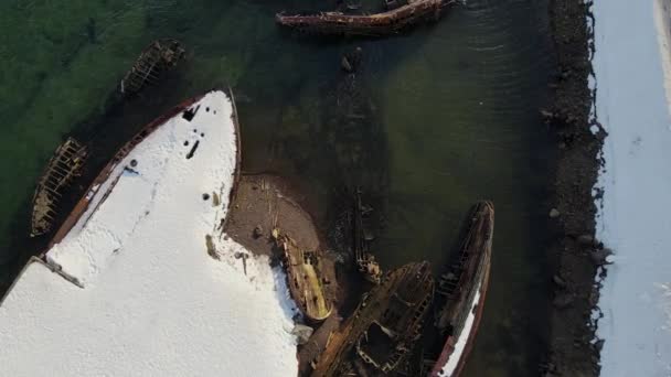 Luftaufnahme alter zerstörter Fischerboote, die in der verschneiten Wintersaison an der Küste ertrunken sind. Verfilmung. Luftaufnahme des zerstörten Bootes im kalten Wasser nahe der verschneiten Sandküste in Teriberka, Russland — Stockvideo