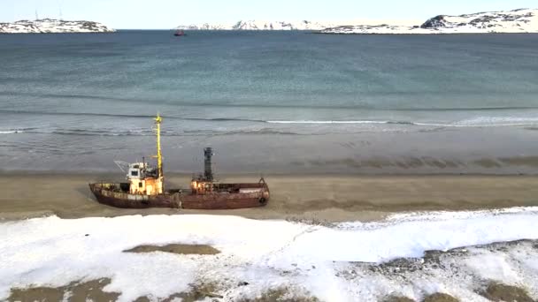 Karlı kış mevsiminde deniz kıyısında boğulan eski batık balıkçı gemilerinin hava manzarası. Görüntü. Rusya 'nın Teriberka kentindeki karlı sahil kıyısındaki soğuk sulardaki harabe teknenin hava görüntüsü. — Stok video