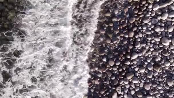 Volo aereo invernale sopra le onde che rotolano sulla riva artica dell'oceano con pietre rotonde, onde oceaniche in tempesta — Video Stock