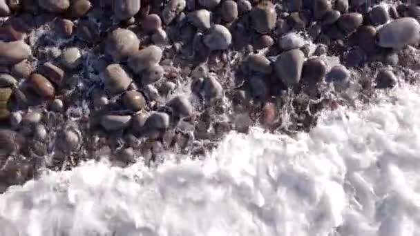 Vuelo aéreo de invierno superior sobre las olas rodando en la orilla ártica del océano con piedras redondas, olas del océano en la tormenta — Vídeos de Stock