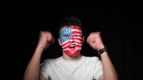 Happy fan rejoices victory of his favorite team of USA. Young man with face painted in national colors of United states of america. Portrait of a happy man supports his national team — Stock Video